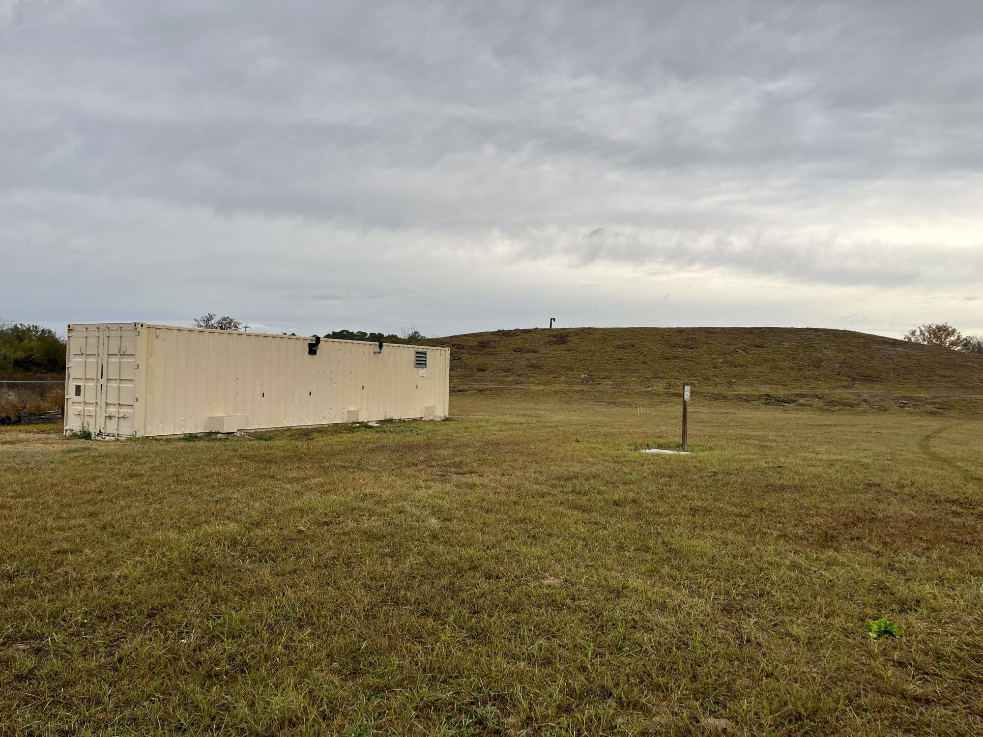 photo of a superfund site with a mound of dirt in the background and a storage unit in the foreground