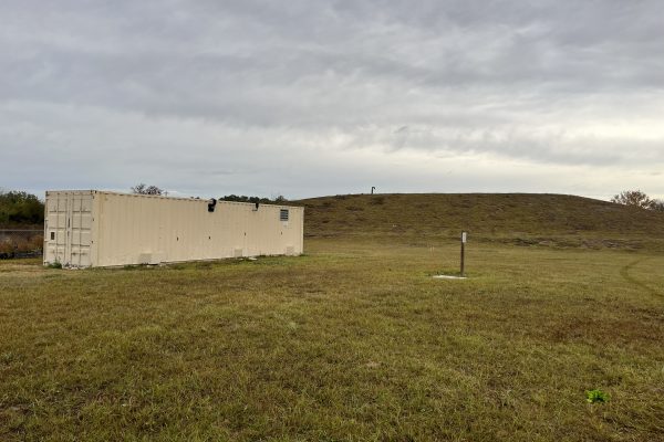 photo of a superfund site with a mound of dirt in the background and a storage unit in the foreground