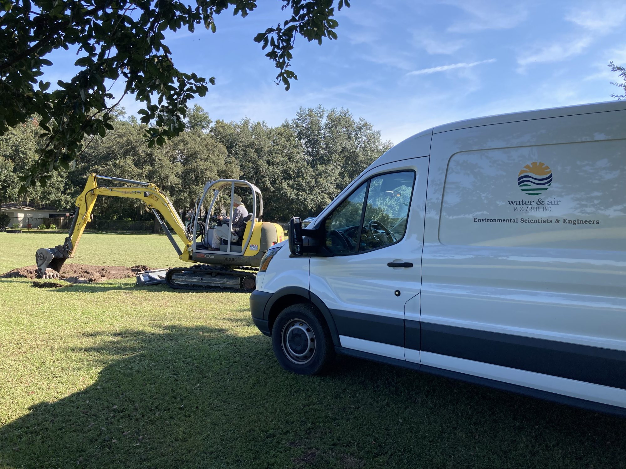 Photo of a work van and a mini excavator digging in a field.