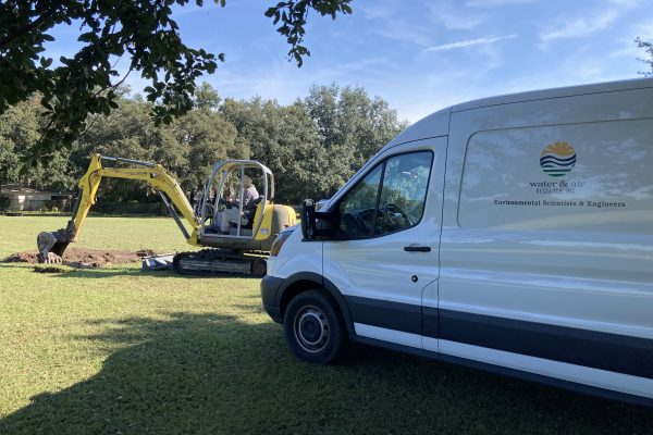 Photo of a work van and a mini excavator digging in a field.